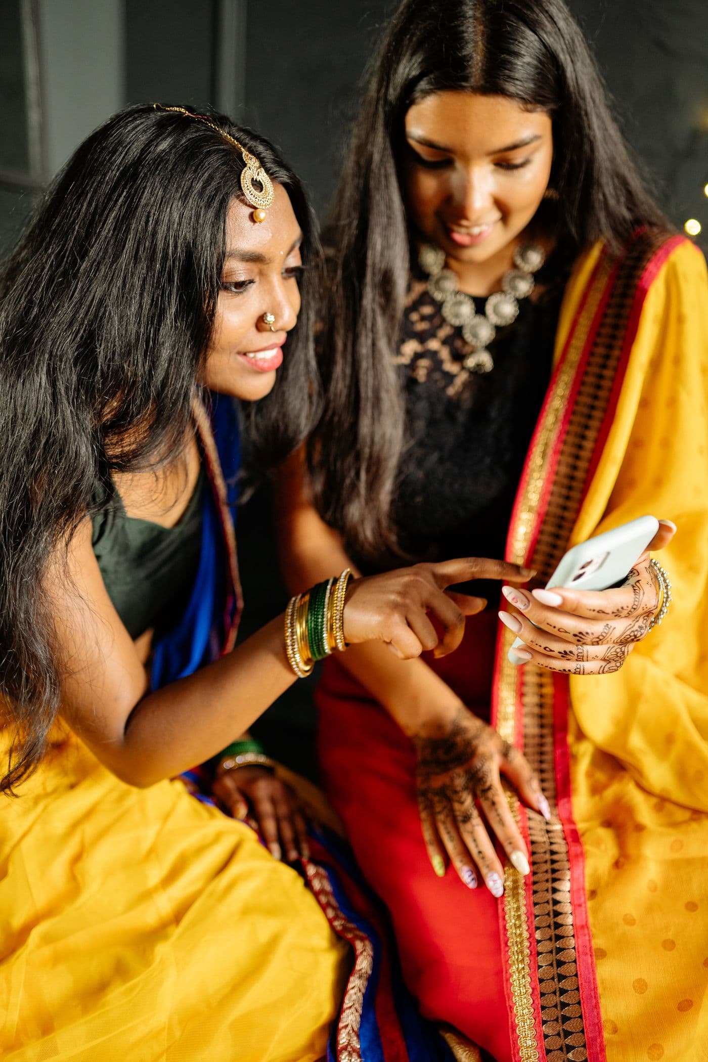 Two women sharing a moment over a phone during an Indian celebration.